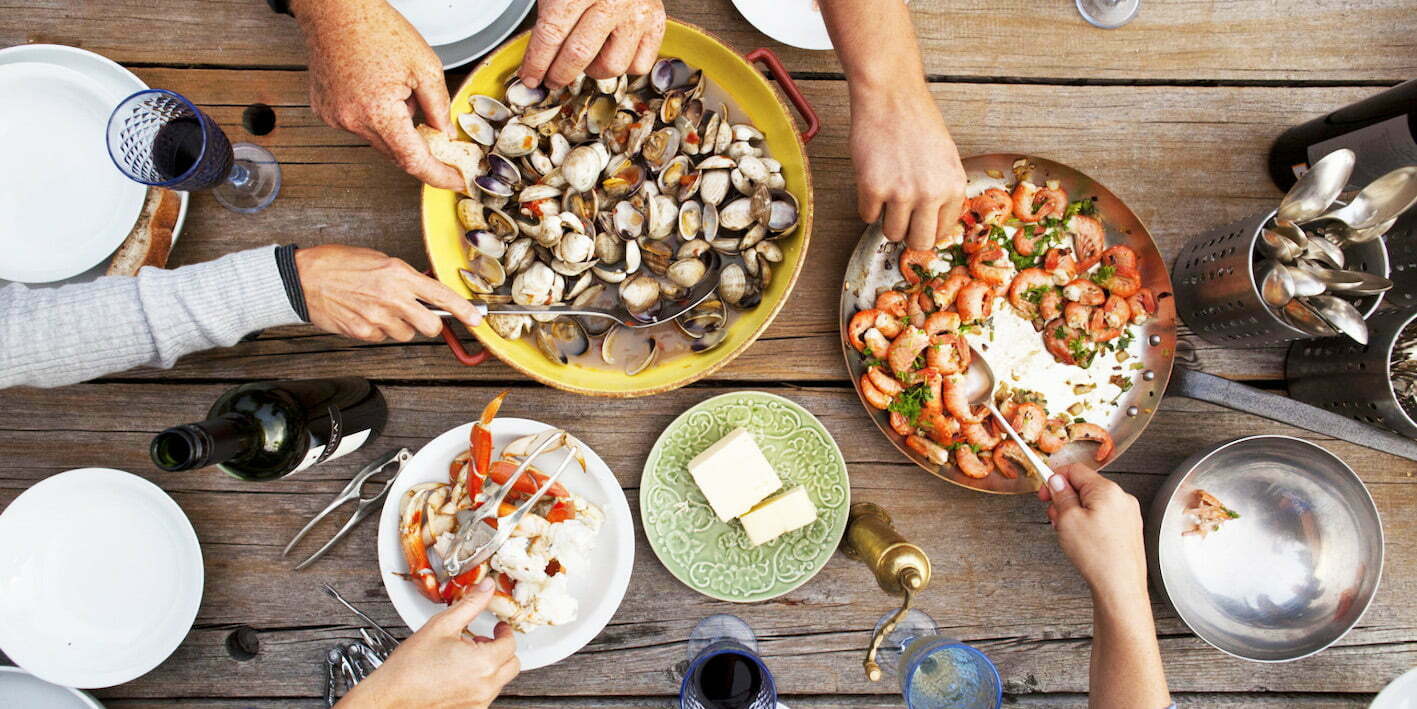 Hands serving shellfish meal around wooden table